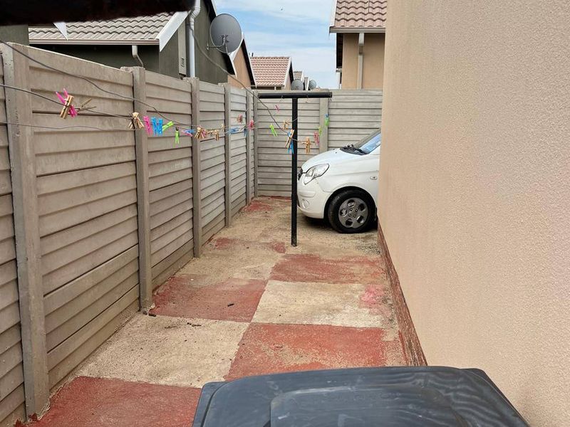 A narrow side yard area featuring a precast concrete boundary wall and painted concrete paving, currently used as a utility space.