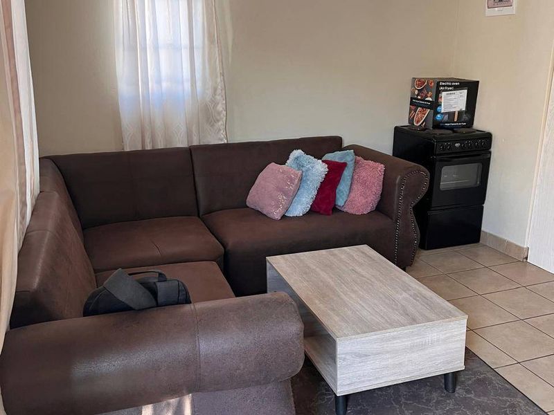 A living room area featuring tiled flooring and a coved ceiling, currently furnished with a corner sofa and a freestanding oven.