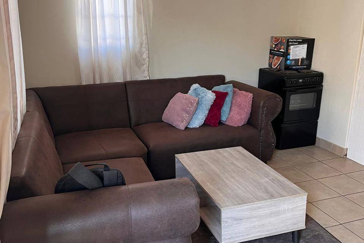 A living room area featuring tiled flooring and a coved ceiling, currently furnished with a corner sofa and a freestanding oven.