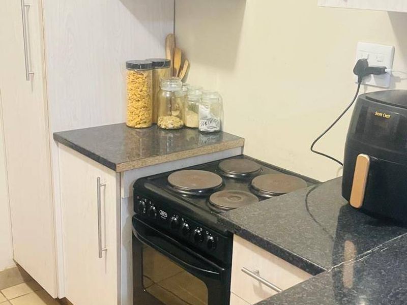 A compact kitchen featuring white cabinetry, dark laminate countertops, and a freestanding electric stove with ceramic tiled flooring.
