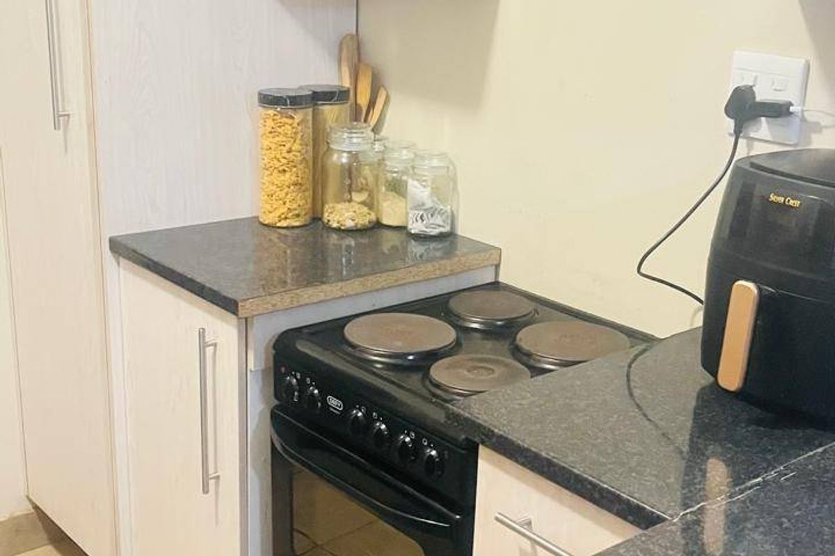 A compact kitchen featuring white cabinetry, dark laminate countertops, and a freestanding electric stove with ceramic tiled flooring.