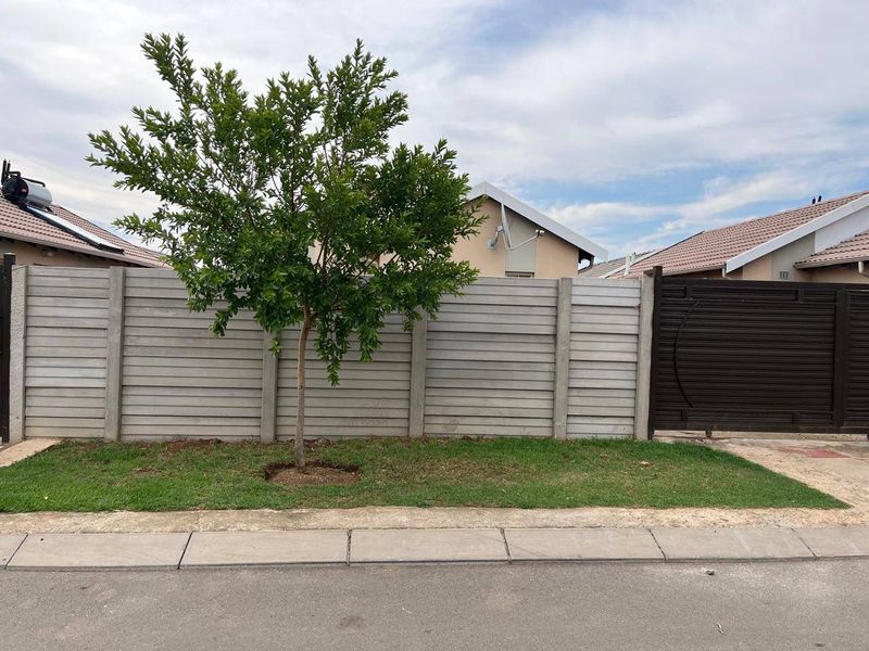 Front view of the property featuring a precast concrete boundary wall, a metal driveway gate, and a neat lawn area.