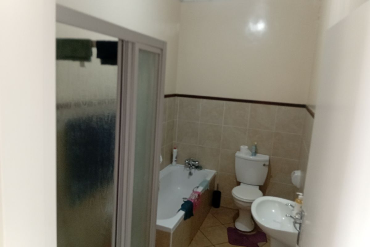 A functional bathroom featuring a bathtub, separate shower enclosure, pedestal sink, and toilet with neutral wall and floor tiling.