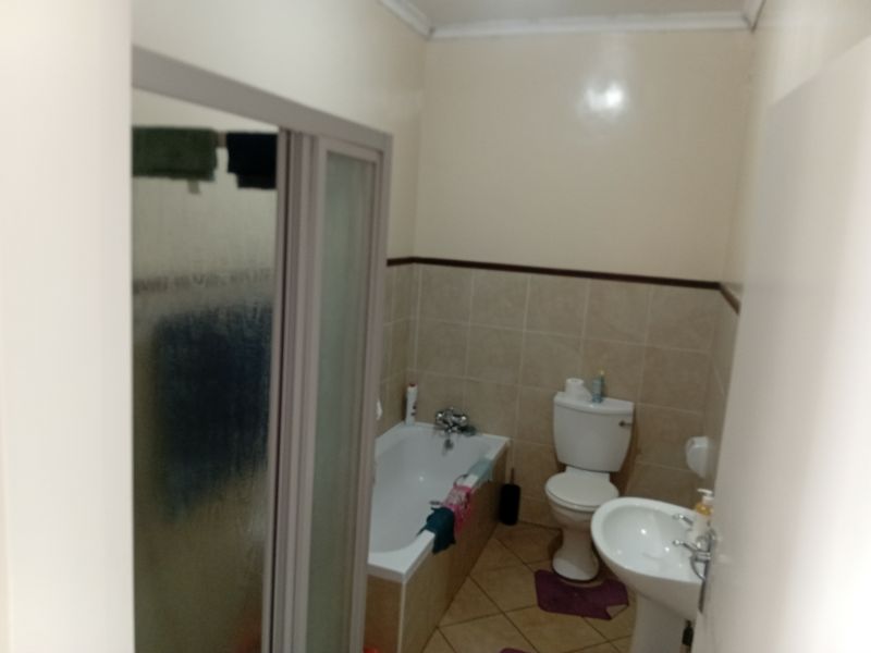 A functional bathroom featuring a bathtub, separate shower enclosure, pedestal sink, and toilet with neutral wall and floor tiling.
