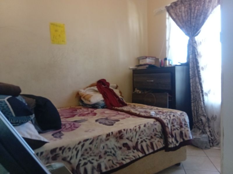 A compact bedroom featuring tiled flooring and a window with curtains, requiring cosmetic updates to improve the overall finish and appeal.