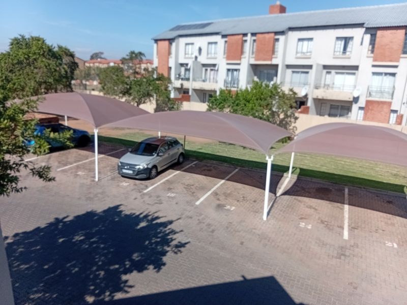 An elevated view of the apartment complex parking area featuring multiple shade cloth carports and paved parking bays.