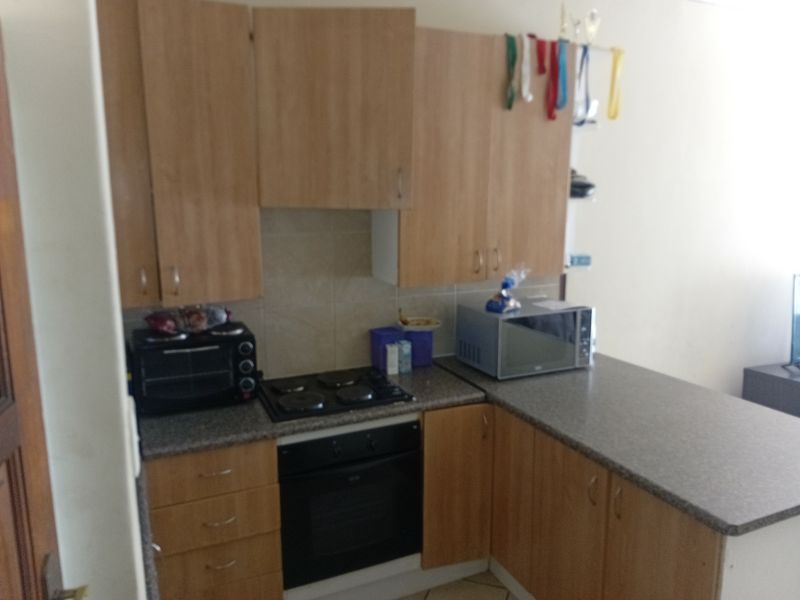 Compact kitchen featuring light wood-tone cabinetry, stone-look laminate countertops, built-in oven, and electric hob with a tiled splashback.