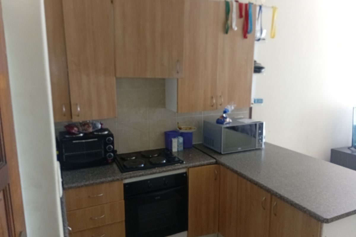 Compact kitchen featuring light wood-tone cabinetry, stone-look laminate countertops, built-in oven, and electric hob with a tiled splashback.