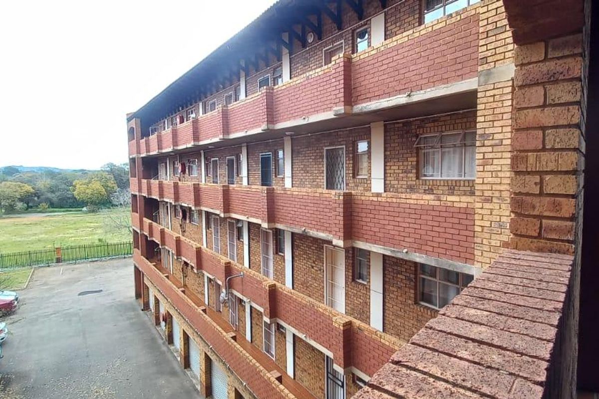 Exterior view of a multi-story apartment building featuring face brick construction, private balconies, and access to ground-level parking areas.
