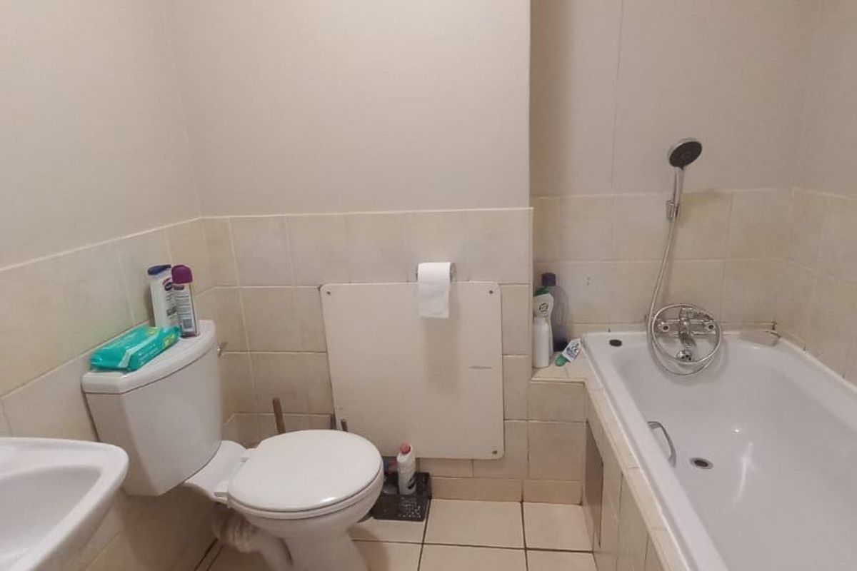 A functional bathroom featuring a bathtub with a handheld shower attachment, a pedestal basin, and a standard toilet with tiled wall and floor finishes.