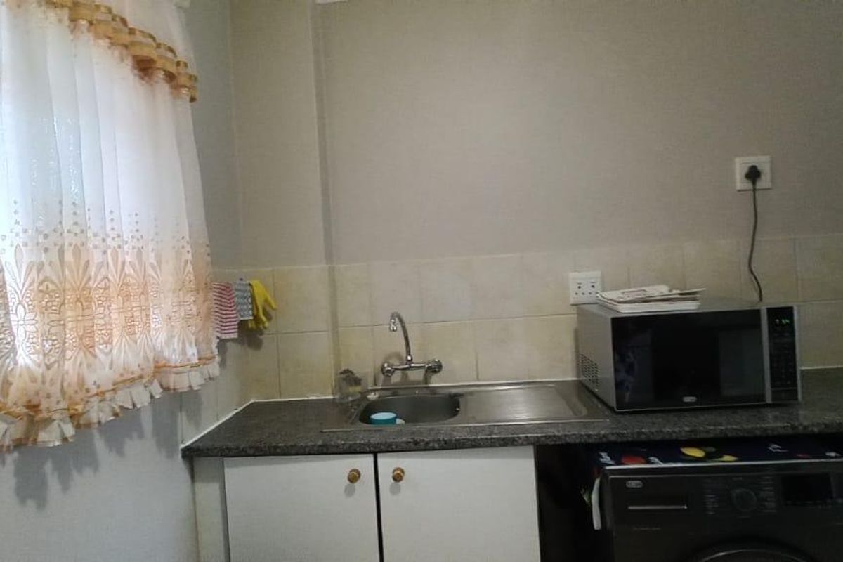 A compact kitchen area featuring a stainless steel sink, tiled splashback, granite countertop, and built-in cabinetry.