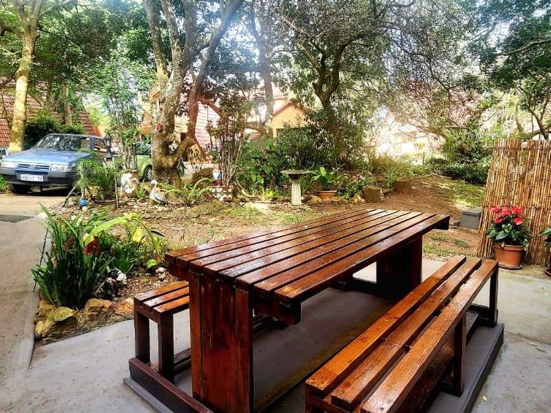 A shaded outdoor patio area featuring a concrete floor, timber staircase, and bamboo privacy screening, set within a mature garden environment.