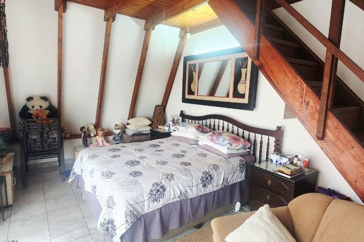 A bedroom featuring exposed timber rafters and a built-in timber staircase leading to an upper level, finished with tiled flooring.