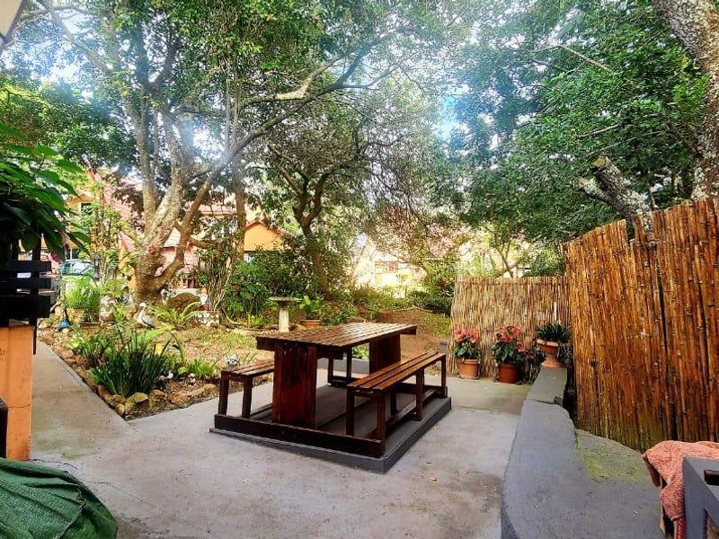 A shaded outdoor patio area featuring a built-in braai, concrete paving, and natural garden surroundings, providing a functional space for outdoor dining and relaxation.