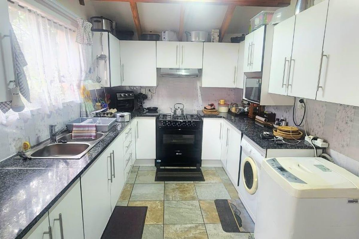 Functional kitchen featuring white cabinetry, granite countertops, gas stove, extractor fan, and tiled flooring with integrated laundry appliance space.