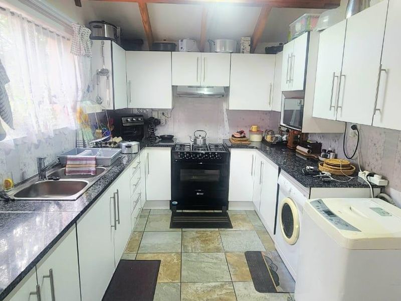 Functional kitchen featuring white cabinetry, granite countertops, gas stove, extractor fan, and tiled flooring with integrated laundry appliance space.