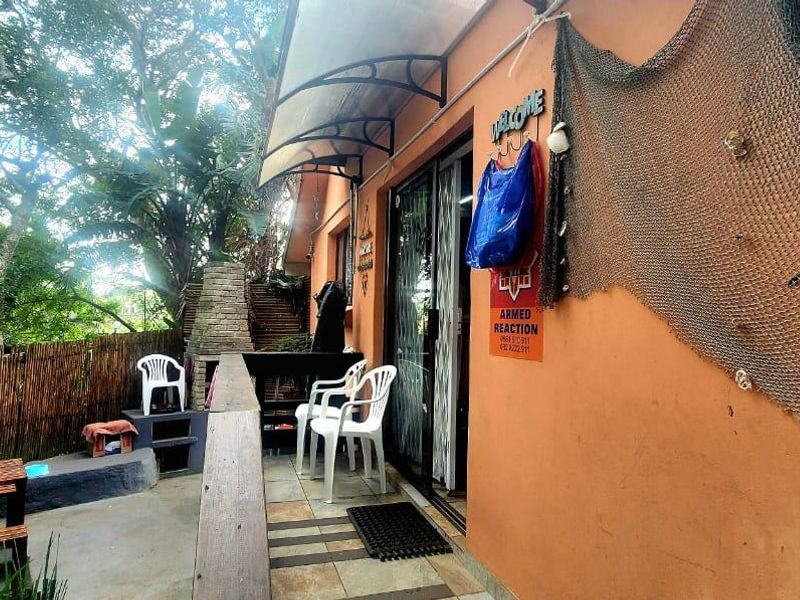Covered outdoor patio area featuring a built-in stone barbecue, tiled flooring, and direct access to the interior through a sliding glass door.
