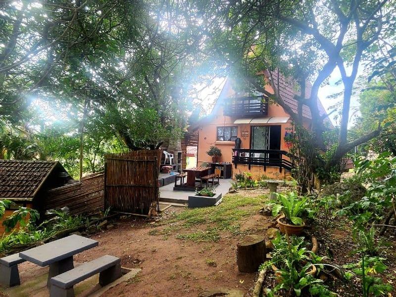 A view of the rear exterior of the townhouse, featuring a balcony, paved patio area, and mature garden surroundings.