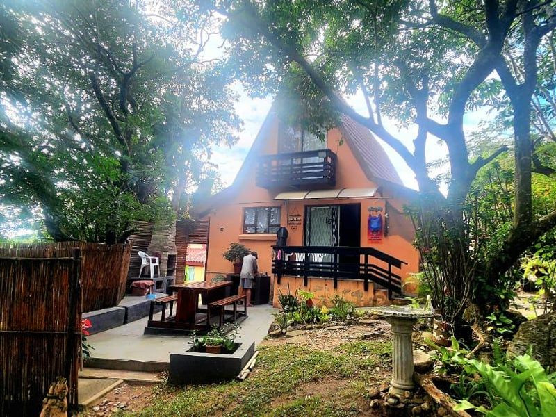 Rear view of a townhouse featuring a private patio area with a built-in braai, balcony, and established garden surroundings.