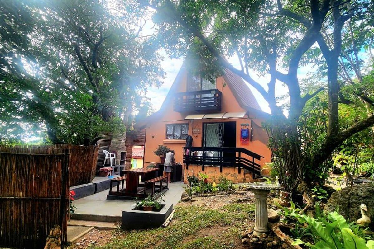 Rear view of a townhouse featuring a private patio area with a built-in braai, balcony, and established garden surroundings.