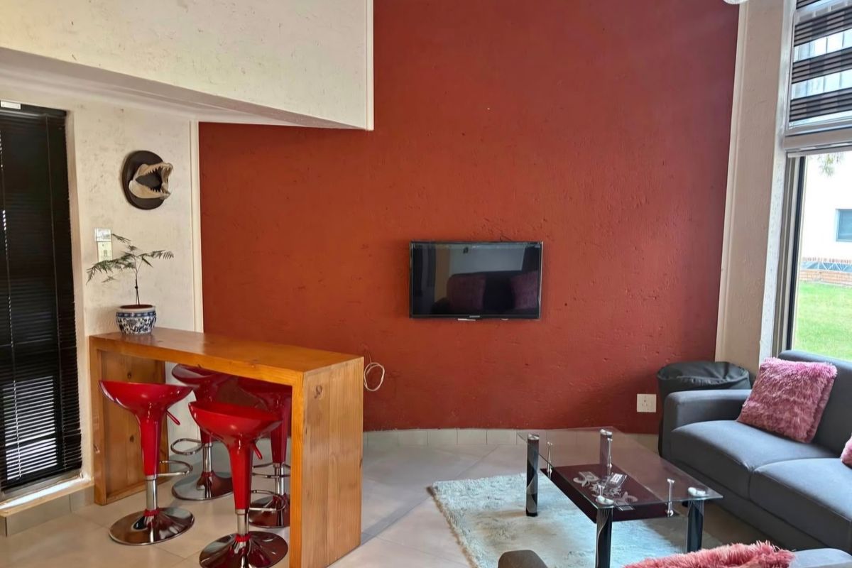 A living area featuring a bold red accent wall, tiled flooring, and a built-in wooden breakfast bar with integrated seating space.