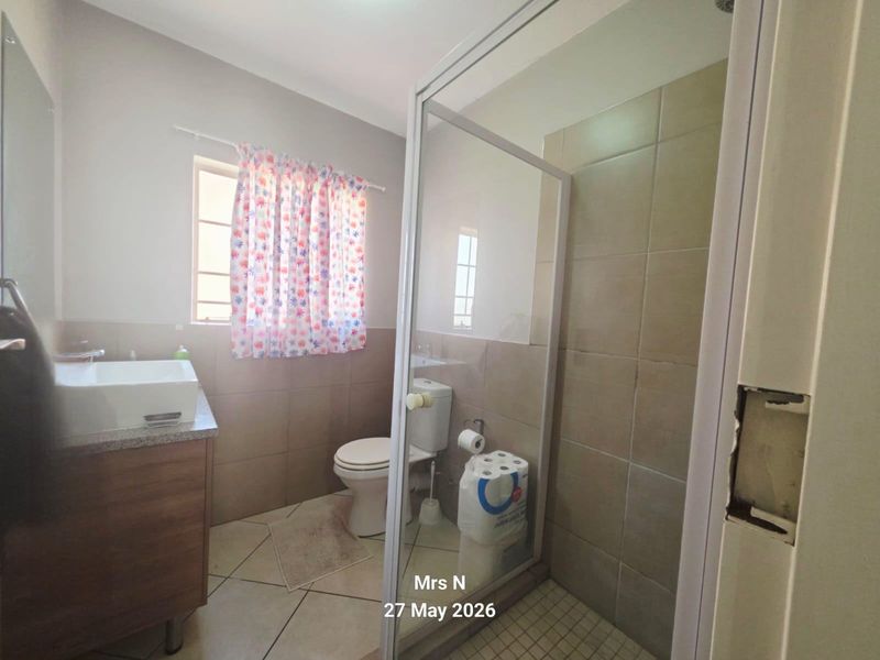 A functional bathroom featuring a shower enclosure, vanity cabinet with vessel sink, and neutral wall and floor tiling.