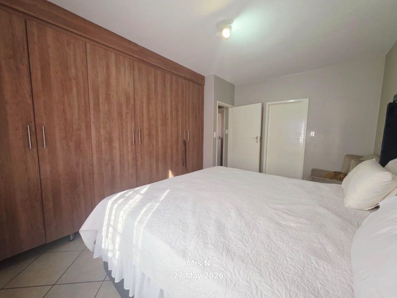 A well-maintained bedroom featuring extensive built-in wooden cupboards and neutral tiled flooring, offering ample storage space.