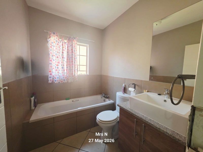A functional bathroom featuring a bathtub, toilet, and a vanity cabinet with a basin. The space includes tiled finishes and a wall-mounted mirror.