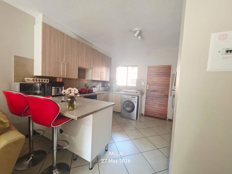 A functional kitchen featuring light wood-finish cabinetry, stone countertops with a breakfast bar, tiled flooring, and a dedicated space for laundry appliances.