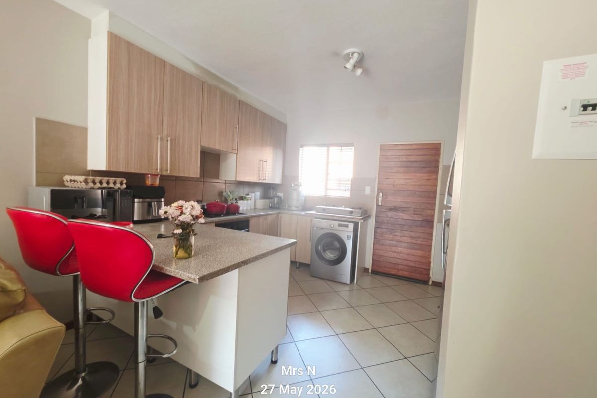 A functional kitchen featuring light wood-finish cabinetry, stone countertops with a breakfast bar, tiled flooring, and a dedicated space for laundry appliances.