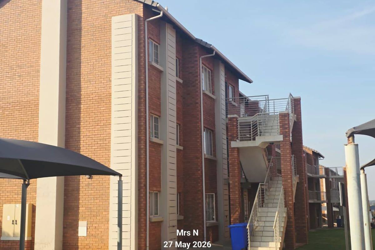 Exterior view of a multi-story apartment building featuring face brick construction, external staircases with metal railings, and paved ground-level walkways.