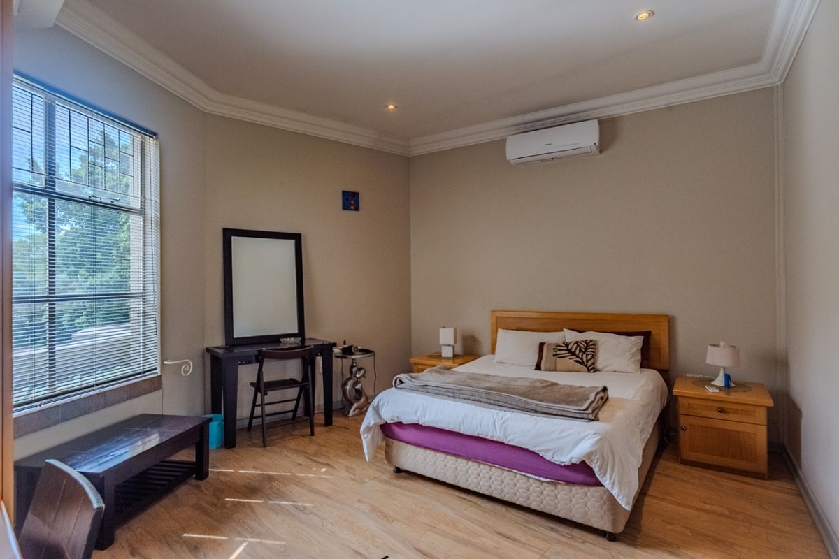 A well-maintained bedroom featuring laminate flooring, coving, recessed lighting, and a wall-mounted air conditioning unit for climate control.