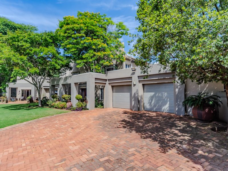 Front elevation of a residential property featuring a double garage, brick paved driveway, and a well-maintained landscaped garden.
