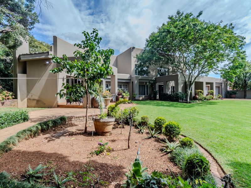 Spacious rear garden featuring a well-maintained lawn, landscaped garden beds with brick edging, and a paved patio area adjacent to the house.