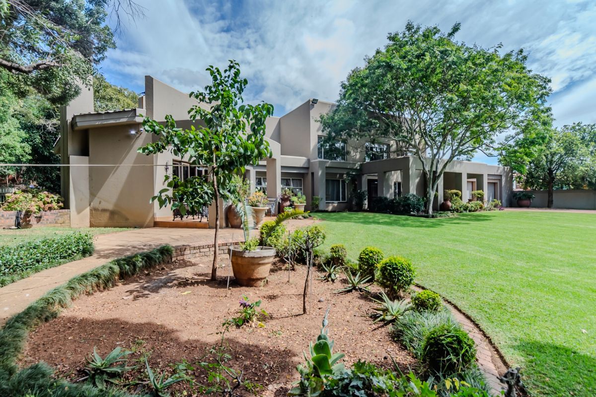 Spacious rear garden featuring a well-maintained lawn, landscaped garden beds with brick edging, and a paved patio area adjacent to the house.