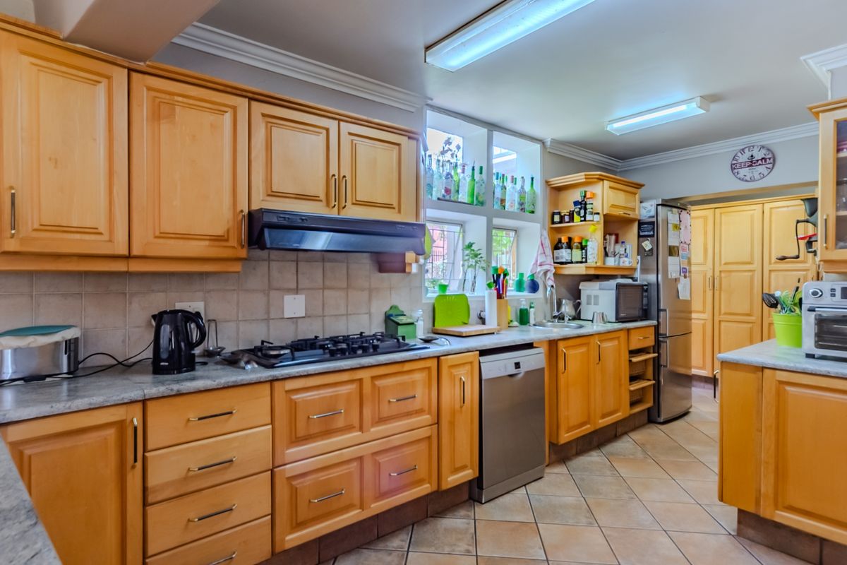 A functional kitchen featuring wooden cabinetry, stone countertops, a gas hob with extractor, and tiled flooring, offering a classic layout with ample storage space.