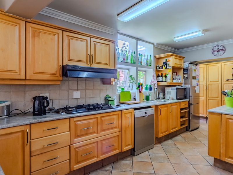 A functional kitchen featuring wooden cabinetry, stone countertops, a gas hob with extractor, and tiled flooring, offering a classic layout with ample storage space.
