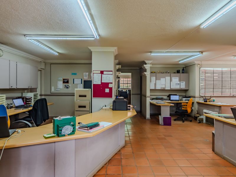 Spacious office area featuring built-in cabinetry, terracotta tile flooring, and functional fluorescent lighting, suitable for a professional workspace or administrative hub.