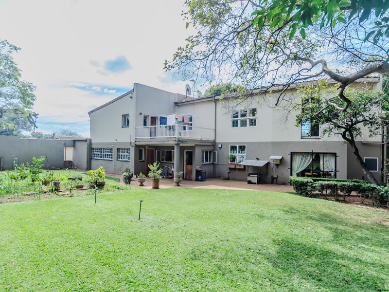 Rear view of the property featuring a spacious lawn, paved patio area, and an elevated balcony with metal railings.