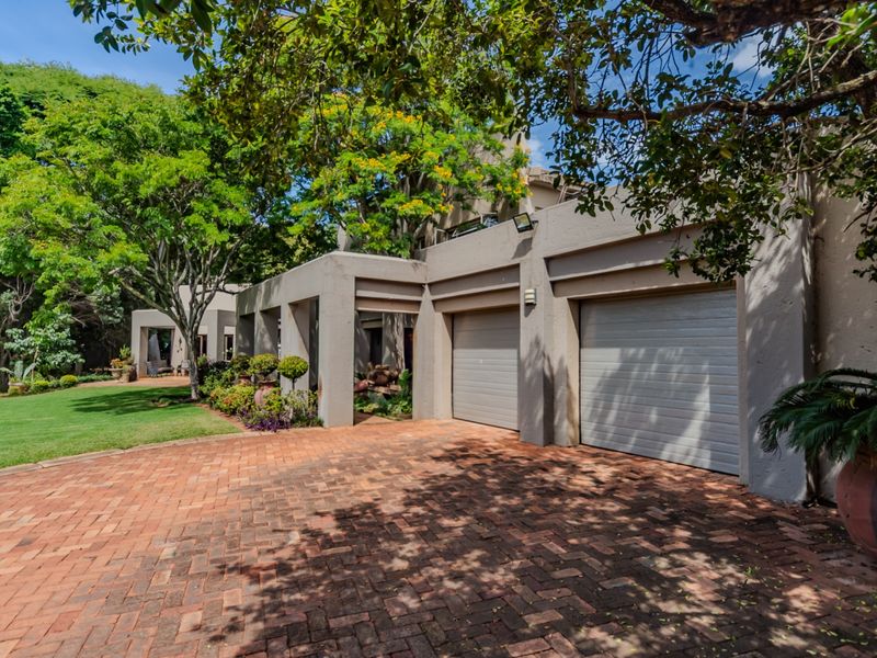 Front elevation of the property featuring a double garage, brick paved driveway, and well-maintained landscaped garden area.