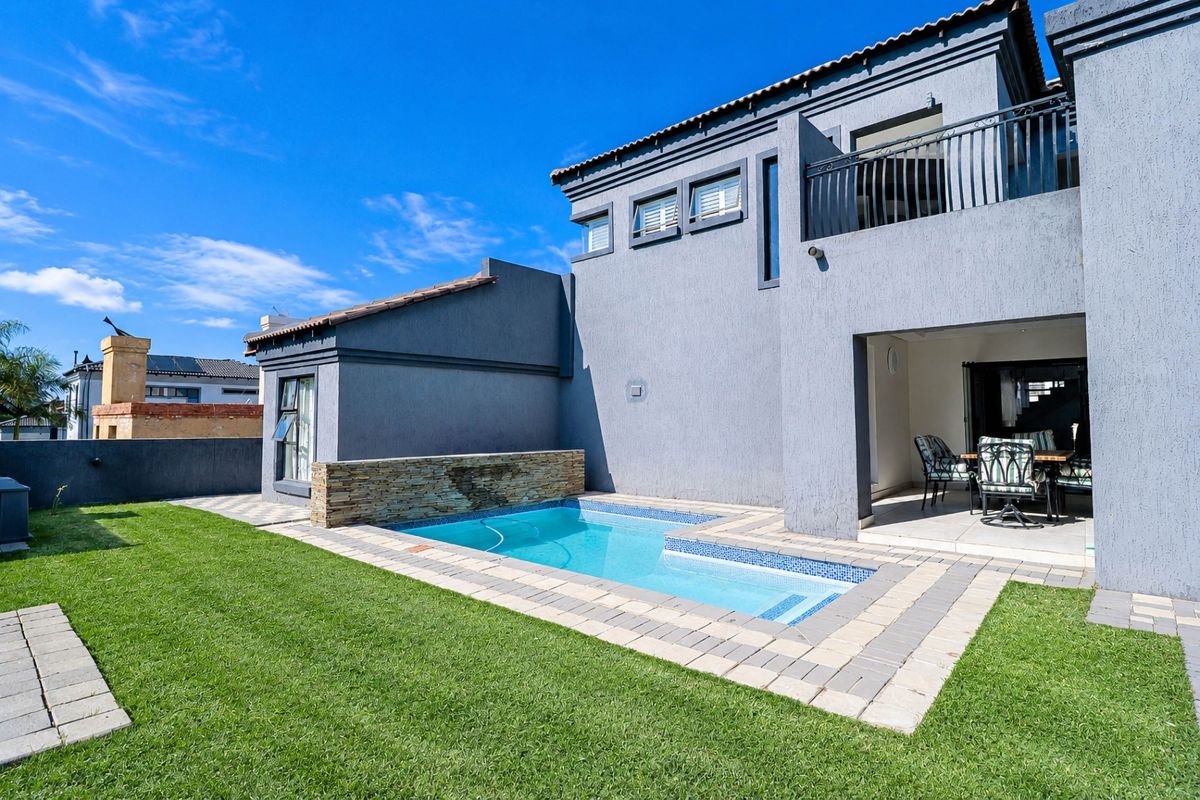 Rear exterior view featuring a swimming pool with a stone feature wall, a covered patio area, and a balcony on the upper level.
