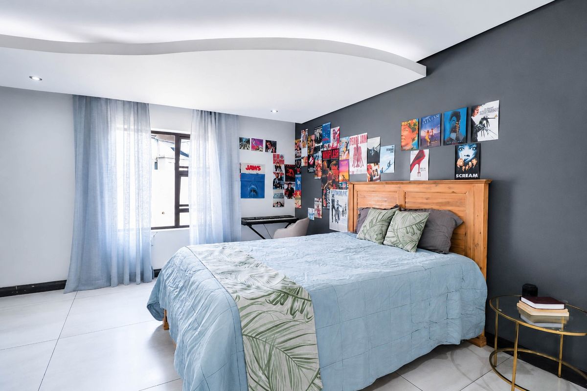 A modern bedroom featuring a unique recessed ceiling design, tiled flooring, and neutral grey accent wall, offering a clean and contemporary living space.