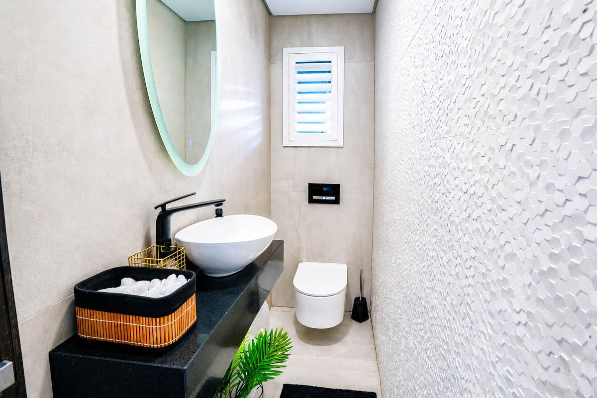 Modern guest bathroom featuring a sleek vessel sink on a black stone vanity, wall-mounted toilet, and a striking textured feature wall.