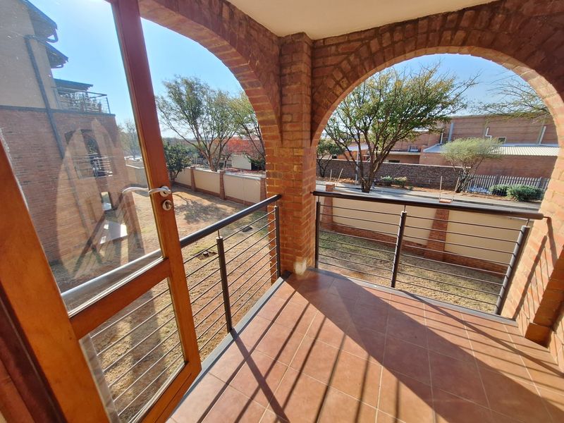 A covered balcony featuring classic brick arches, tiled flooring, and a metal balustrade, offering an open view of the surrounding complex grounds.