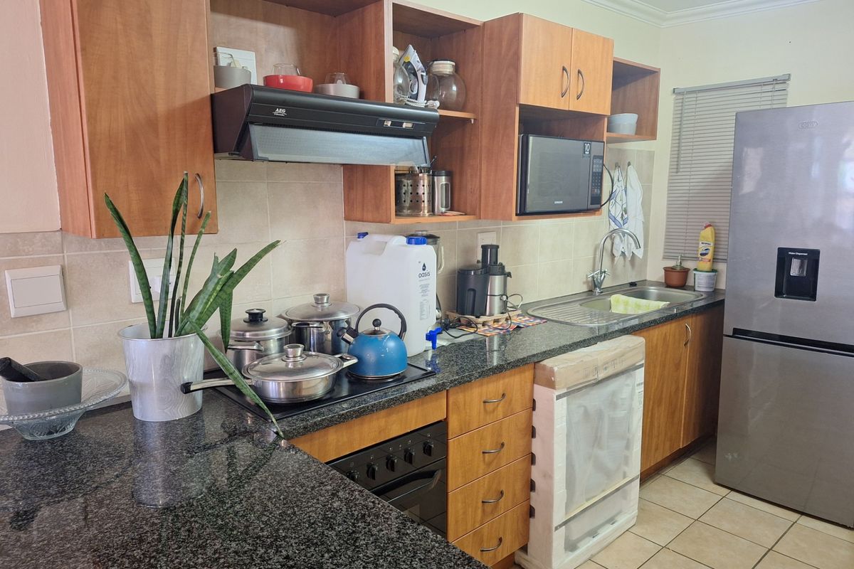 Functional kitchen featuring granite countertops, wooden cabinetry, built-in oven, hob, extractor fan, and integrated microwave, finished with tiled flooring.
