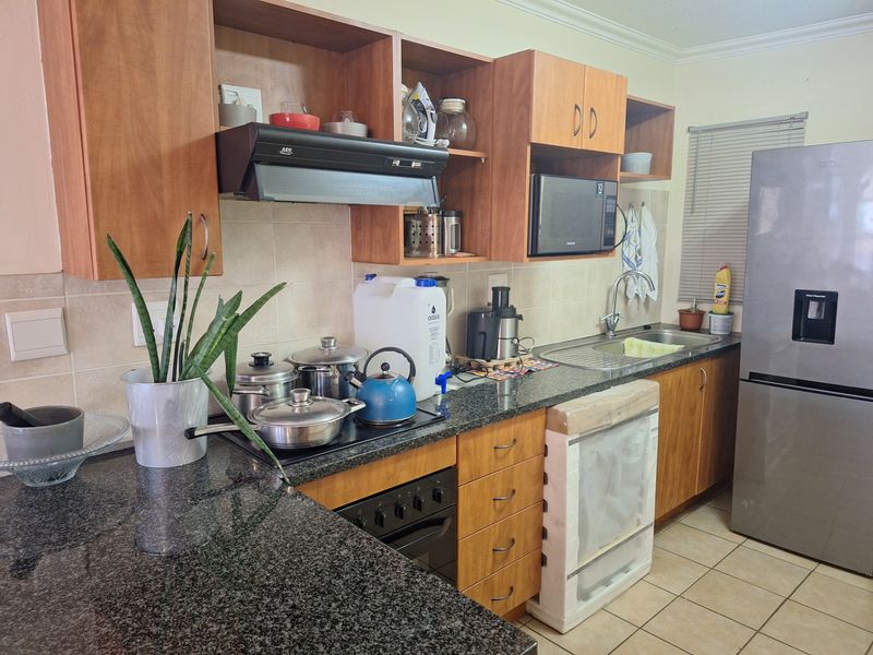 Functional kitchen featuring granite countertops, wooden cabinetry, built-in oven, hob, extractor fan, and integrated microwave, finished with tiled flooring.