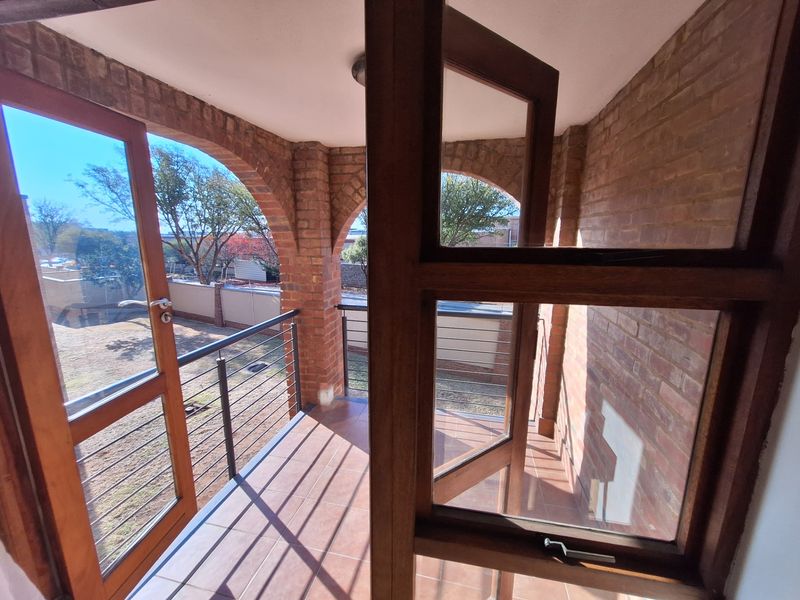 A covered balcony featuring brick arches, tiled flooring, and timber-framed glass doors, offering an open-air space with a metal balustrade.