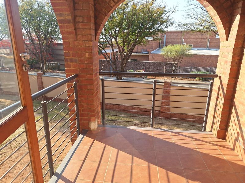 A covered balcony featuring a classic brick archway, tiled flooring, and a modern metal balustrade overlooking the surrounding grounds.