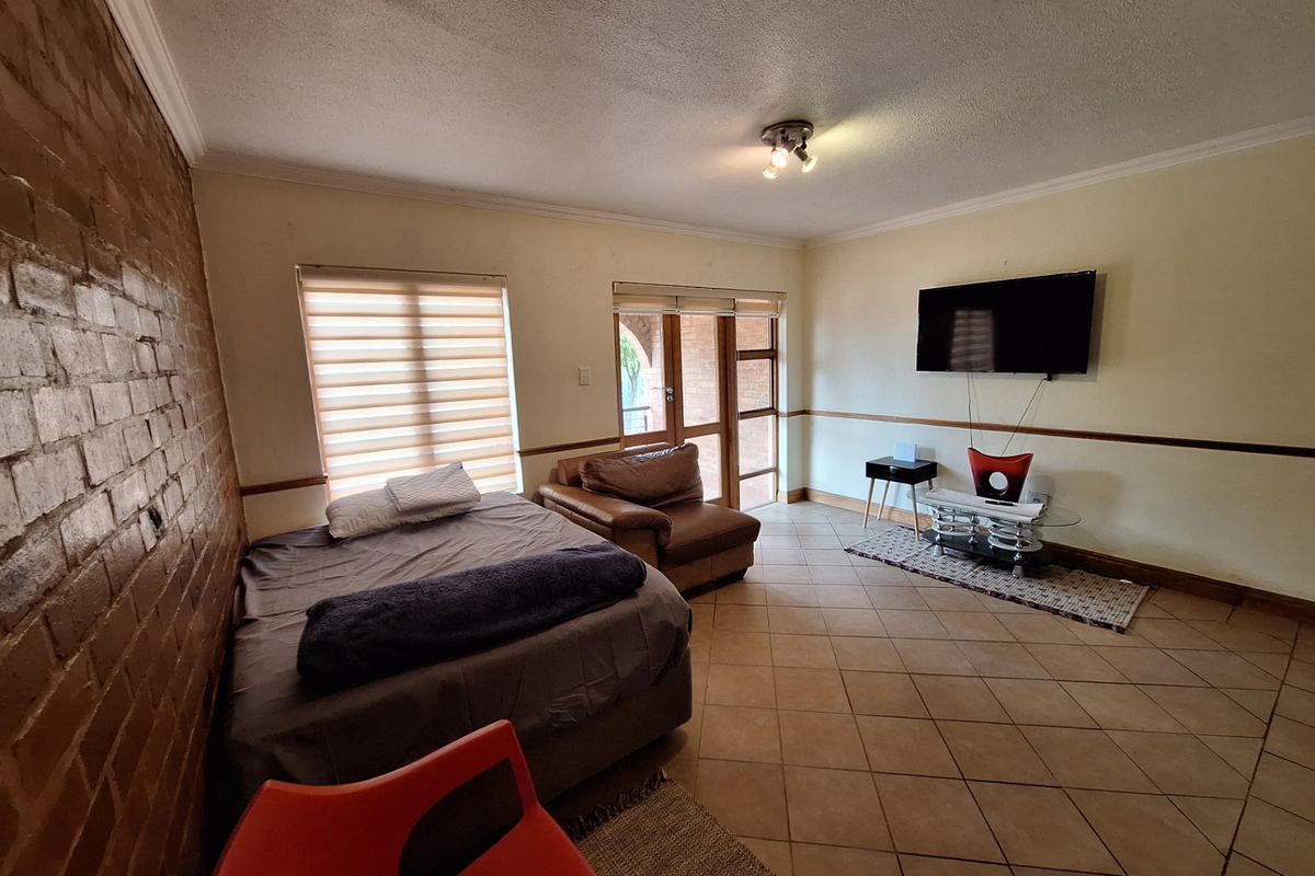 Spacious living area featuring an exposed brick feature wall, ceramic tiled flooring, and direct access to an outdoor patio area.