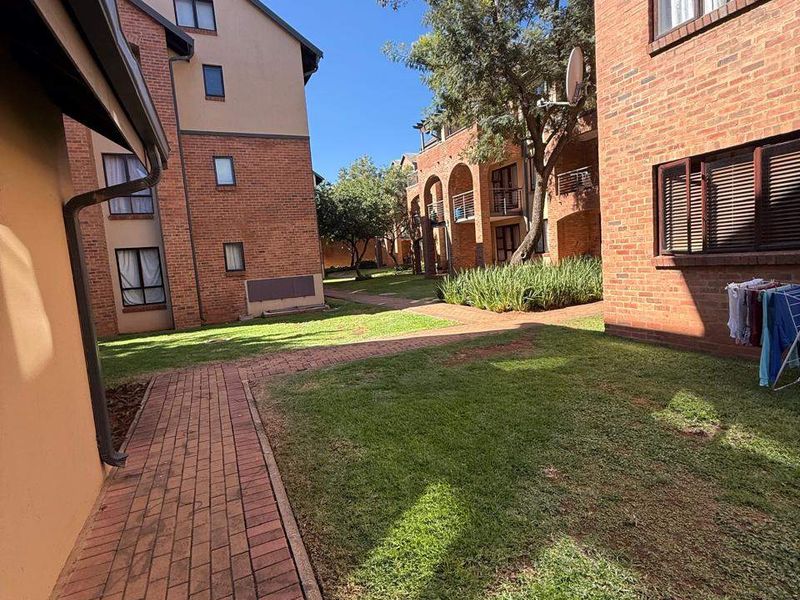 A view of the communal garden area between apartment blocks, featuring brick paved pathways and well-maintained lawn and landscaping.